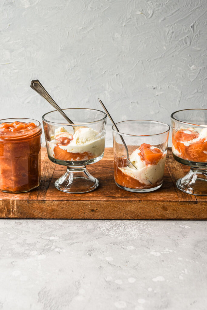 Glass jars in a row with vanilla ice cream and peach compote on top.