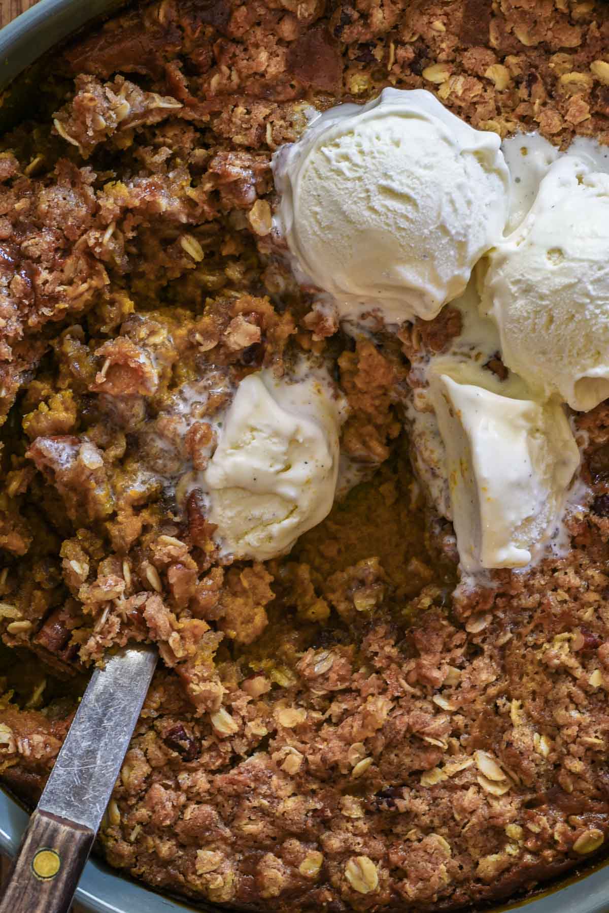 Pumpkin crisp with a spoon and melting ice cream.